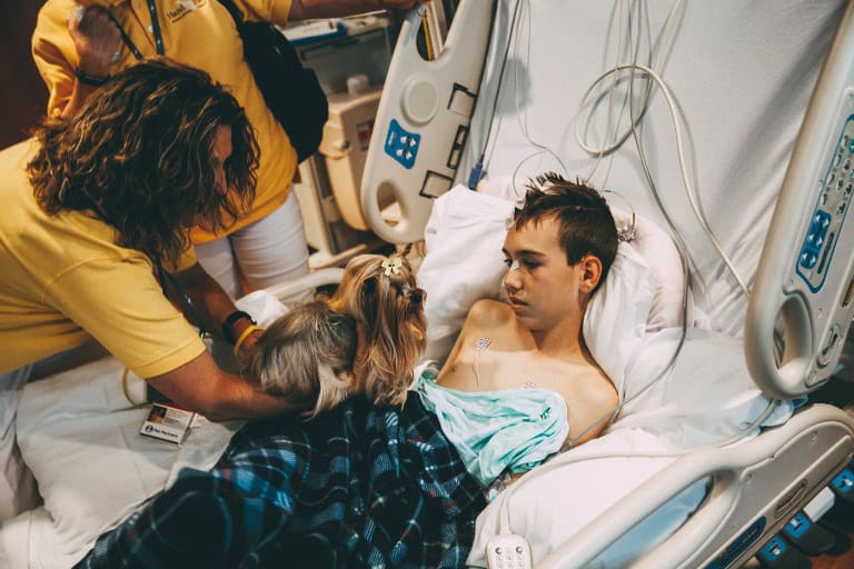 Therapy dog visits a child in a hospital room with its handler.