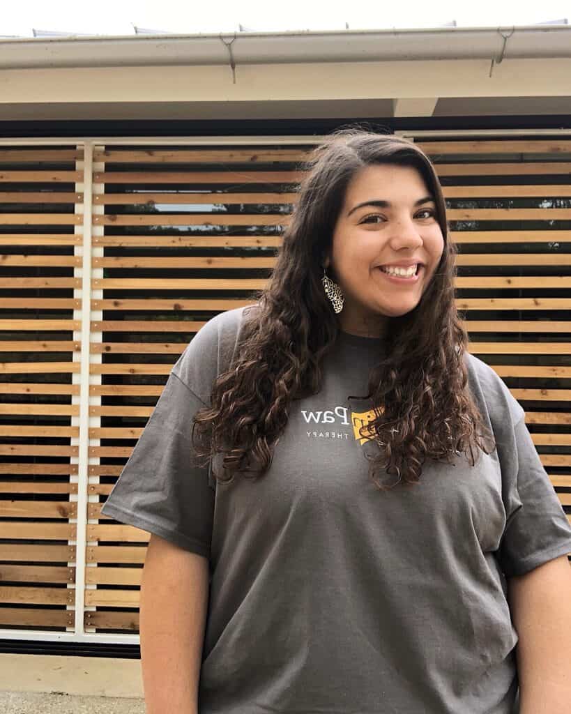 Catherine, a Hand in Paw intern, smiling in a branded T-shirt outside.