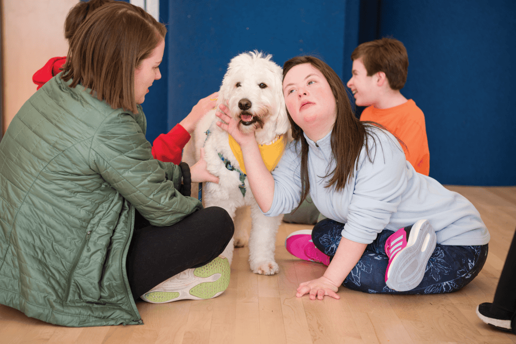 Children and adults interact with a therapy dog during a Hand in Paw school visit.