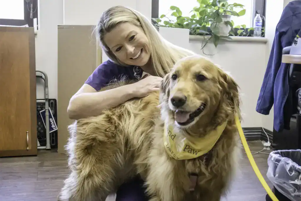 Hand in Paw volunteer with a golden retriever Therapy Team dog in an indoor care setting.