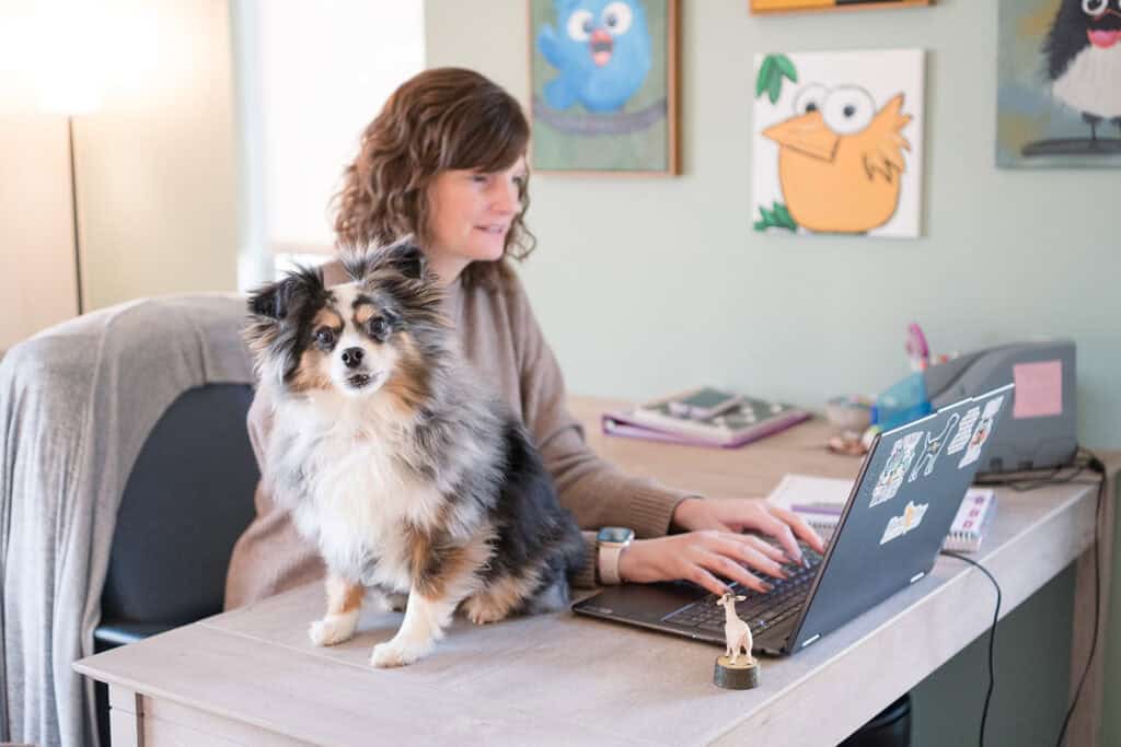 Amanda Summers works at a desk with her dog beside her.
