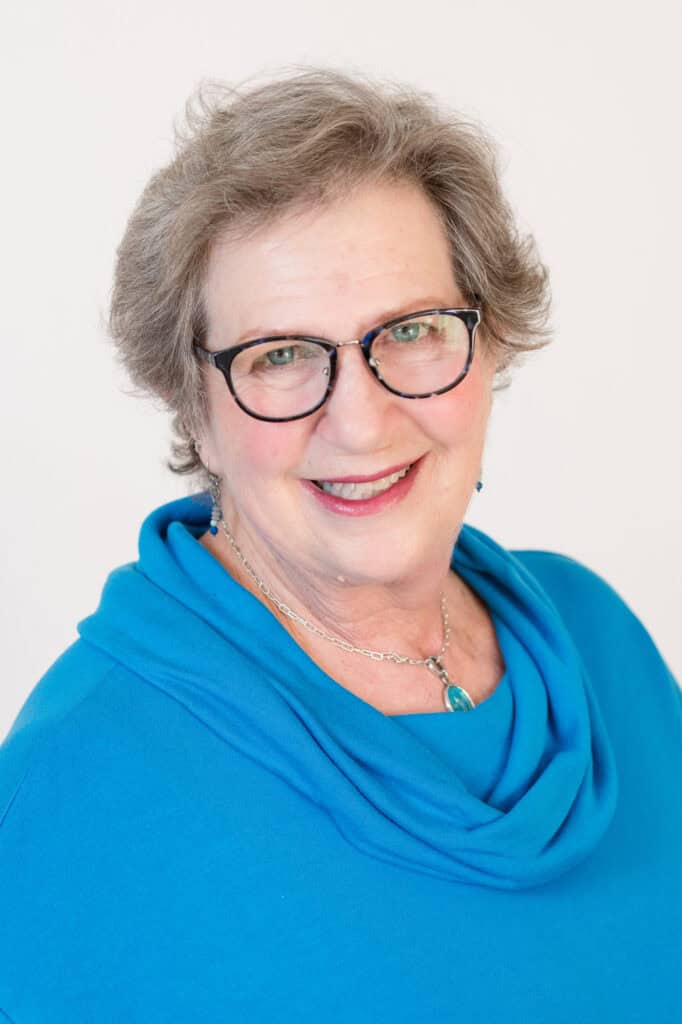 Portrait of Carol DeVelice, a smiling Hand in Paw team member wearing glasses and a blue top.