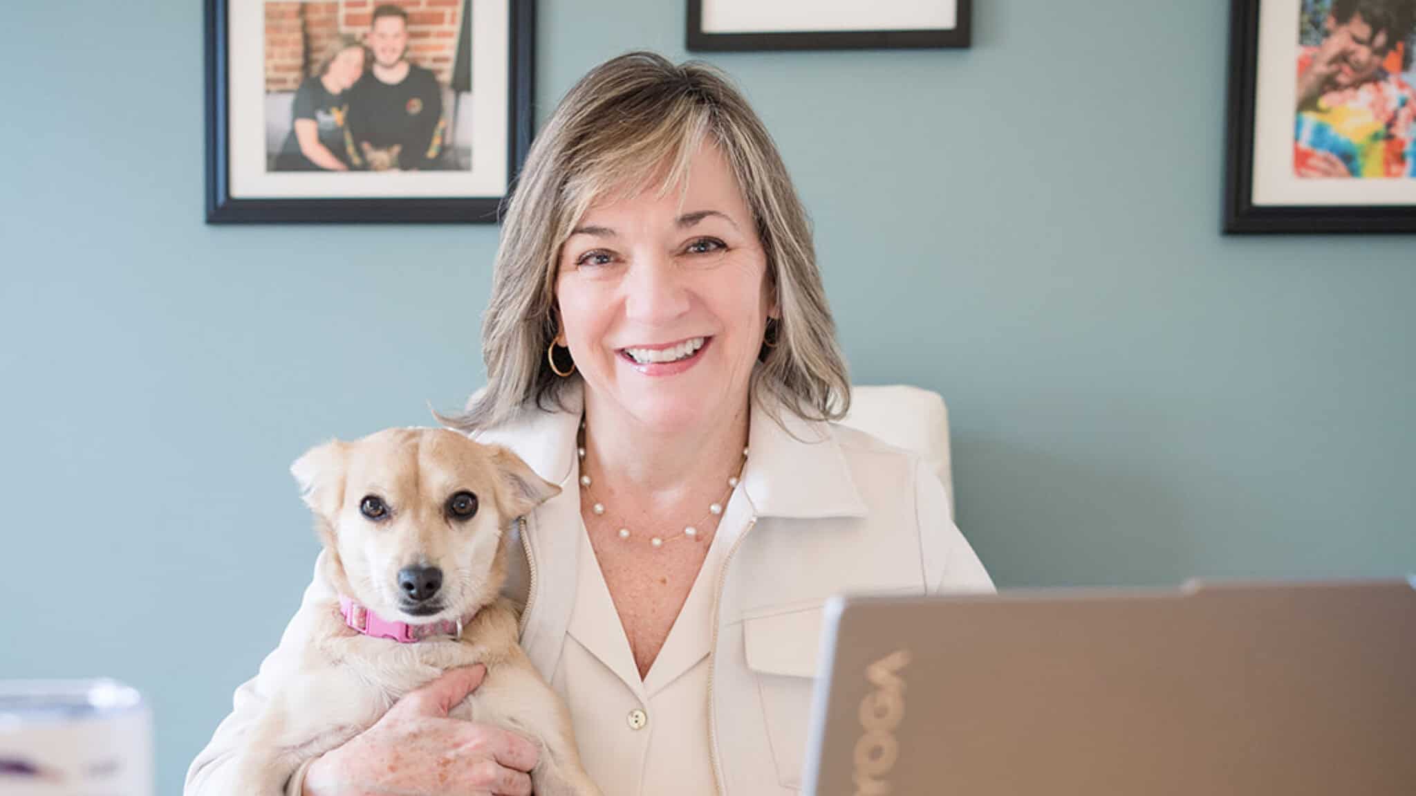 Hand in Paw volunteer holding a therapy dog beside a laptop