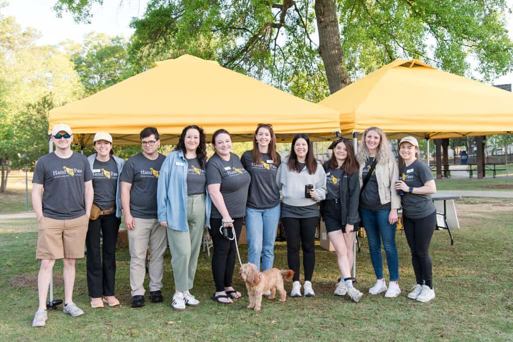 Hand in Paw volunteers and a therapy dog gather beneath event tents at the Mutt Strut.