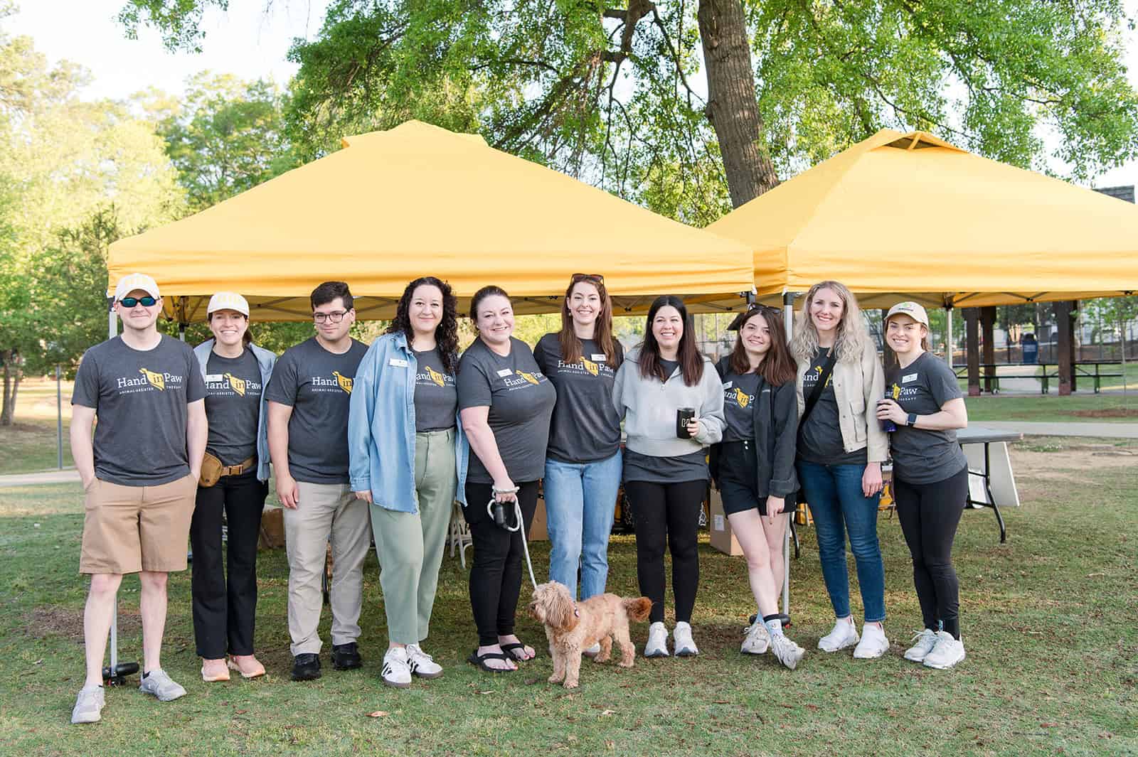 Hand in Paw volunteers and a therapy dog gather beneath event tents at the Mutt Strut.