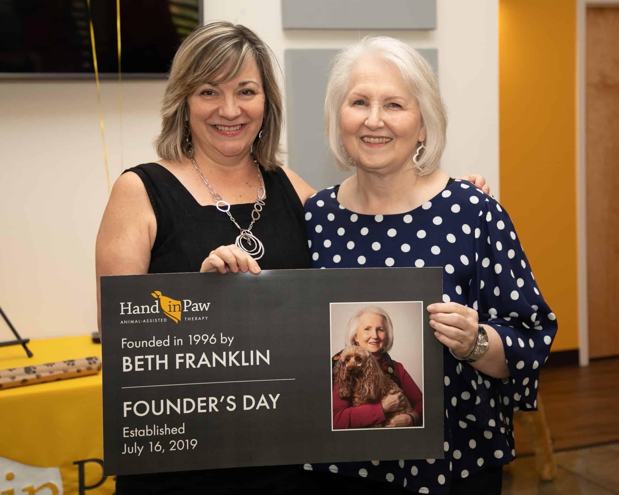 Two women hold a Hand in Paw Founder’s Day plaque honoring founder Beth Franklin.