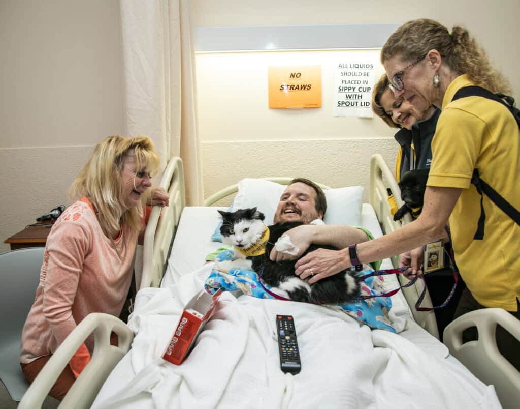 Therapy Team volunteers visit a hospital patient with a cat during animal-assisted therapy.
