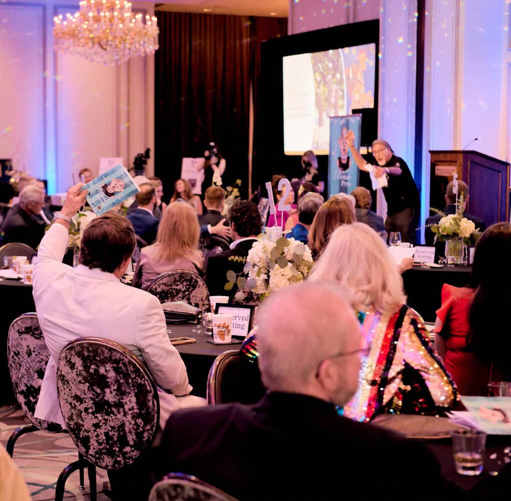 Audience members participate in a formal community event presentation with a speaker at the front.