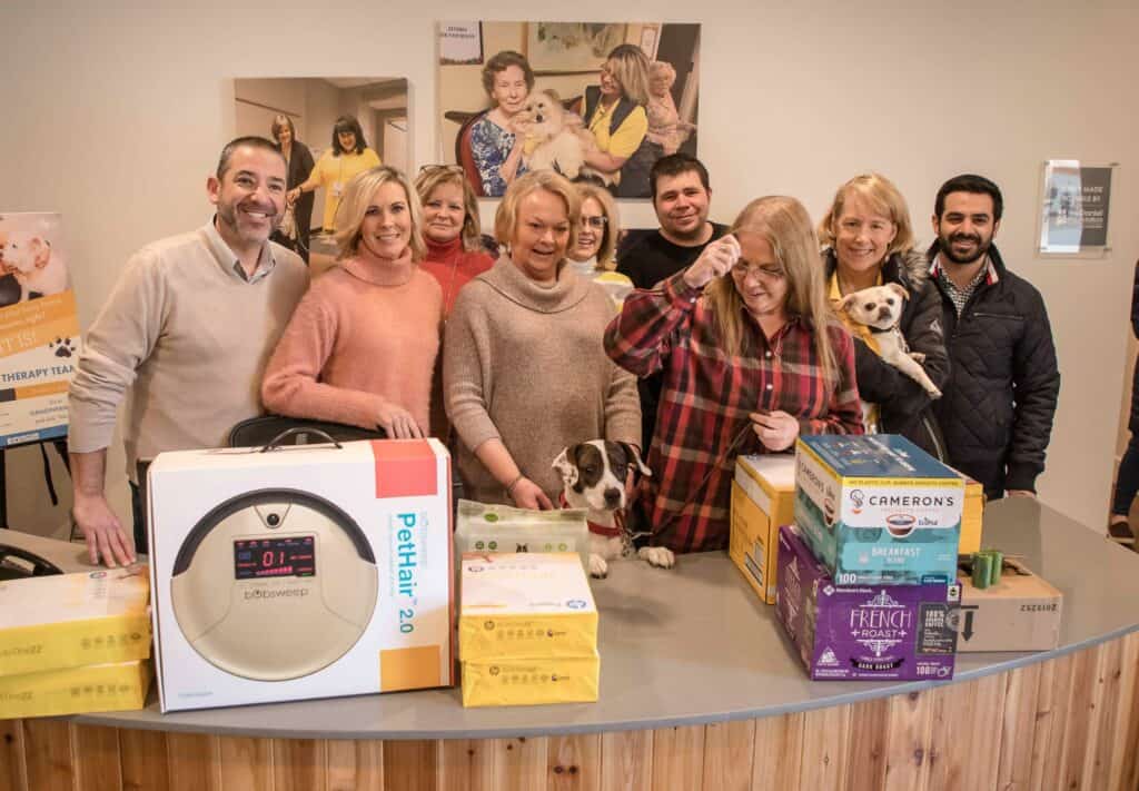 Hand in Paw volunteers and therapy dogs gather with donated pet food and supplies.