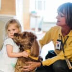 Therapy dog and handler comfort a young child in a care setting.